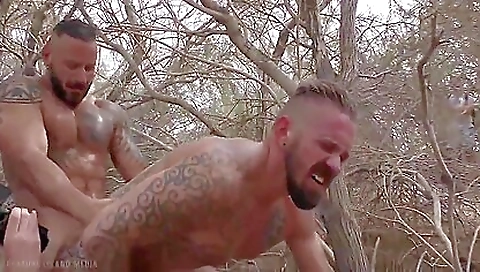 Two men in the open field of the desert sucking the cum
